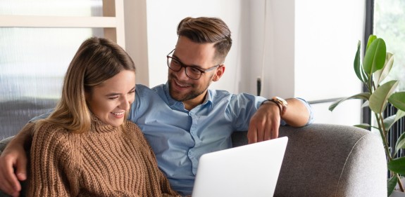 Pärchen sitzt auf der Couch und recherchiert am Laptop
