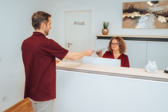 Hr. Bice überreicht Fr. Engelhardt ein Dokument an der Anmeldung